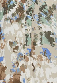 Silkesblus med en beige bas och abstrakta mönster i olivgrön, brun och blå. Fyra gyllene knappar framtill.