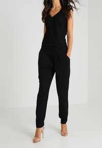 Black sleeveless top with a textured pattern and V-neck, paired with tapered black pants featuring side pockets and a smooth fabric finish.