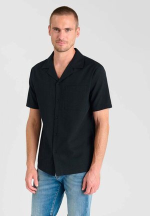 Korte mouw, gekraagde shirt van effen zwarte stof, voorzien van een borstzak en knoopsluiting, gecombineerd met lichtblauwe jeans.