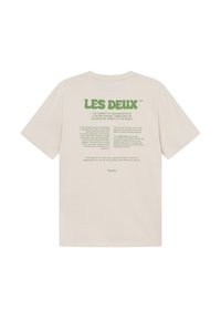 Rövid ujjú bézs póló, zöld nyomott szöveggel a hátán, beleértve a márkanevet és grafikai elemeket. Puha pamut anyag.