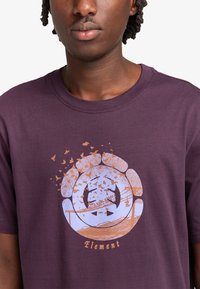 Purple cotton t-shirt featuring a circular graphic with birds and landscape designs in orange and blue, accented by the word "Element."