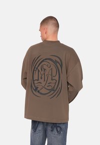 Übergroßer brauner Sweatshirt mit einem großen schwarzen Grafikdesign auf dem Rücken, langen Ärmeln und Rundhalsausschnitt.