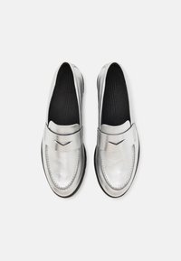 Mocassins argentés en cuir métallique lisse, avec un bout rond et une couture décorative. Équipés d'un semelle noire et d'un accent rectangulaire sur la sangle.