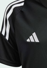 Čierne športové tričko s bielymi pruhmi na pleciach a vyšitým bielym logom s tromi pruhmi na hrudi. Hladká textúra, krátke rukávy.