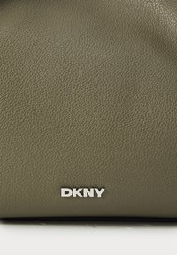 Olivia vihreä nahkakäsilaukku, jossa on teksturoitu pinta ja hopeinen "DKNY" -logo. Ominaisuuksina yksinkertainen muotoilu ja rakenteellinen muoto.