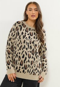 Beżowy sweter z wzorem w panterkę w kolorze czarnym i brązowym, z okrągłym dekoltem i długimi rękawami, wykonany z miękkiego materiału o fakturze.