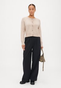 Bežna cardigan iz volne z mešanico, okroglo izrezan, z rebrastimi manšetami in šestimi gumbi. V kombinaciji s črnimi hlačami širokega kroja in torbico z črtami.