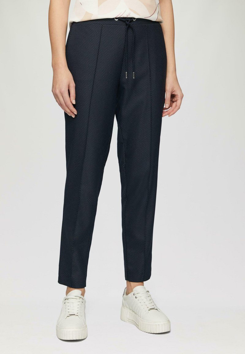 Pantalon bleu marine avec un motif à pois, design tapered, taille élastique avec cordon de serrage, et plis subtils, associé à des baskets blanches.