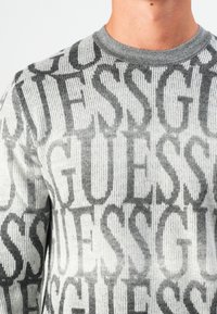 Maglione grigio e bianco con texture a costina e pattern ripetuti "GUESS" in varie tonalità, con collo a girocollo e finitura di alta qualità.