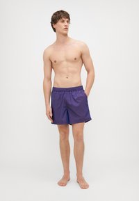 Pantaloni da bagno viola con cintura elastica e tasche laterali, realizzati in un tessuto leggero e morbido, aderenti al corpo senza motivi.