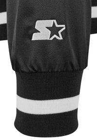 Vêtements de sport noirs avec emblème blanc et rayures horizontales. Comprend des poignets côtelés et une texture lisse, soulignant les éléments de design sportif.