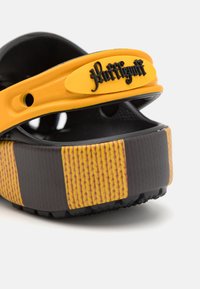 Gul och svart slip-on sandal med texturerad svart sula, räfflad rem och mönstrade sidopaneler. Har en logotyp på remmen.