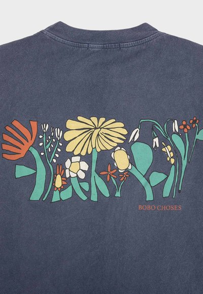 Tissu bleu foncé avec un imprimé floral abstrait coloré en orange, jaune, blanc et vert, et le texte « BOBO CHOSES » en orange.