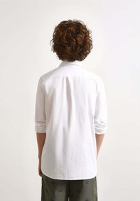 Witte lange mouwen shirt met opgerolde manchetten, zachte stof, achteryoke-detail, gecombineerd met gestreepte groene broek.