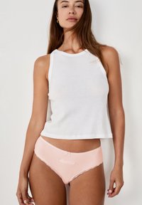 Un débardeur blanc sans manches avec un col rond, associé à un sous-vêtement rose clair ornés de dentelle et d'un petit nœud au niveau de la taille.