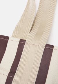 Borsa tote a righe con colori alternati marrone e crema. Realizzata in tessuto resistente con manici spessi e cuciture rinforzate.