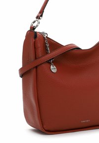Sac à bandoulière en cuir marron texturé avec chaîne argentée et étiquette métallique ronde, avec le nom de la marque Suri Frey sur le devant.