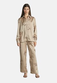 Ensemble de pyjama en satin beige, featuring broderie florale et une chemise à boutons à manches longues, associée à un pantalon à coupe décontractée.