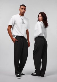 T-shirt graphique blanc avec impression "Style Gothique", associé à un pantalon noir à fines rayures. Le modèle porte des baskets noires avec des accents blancs.
