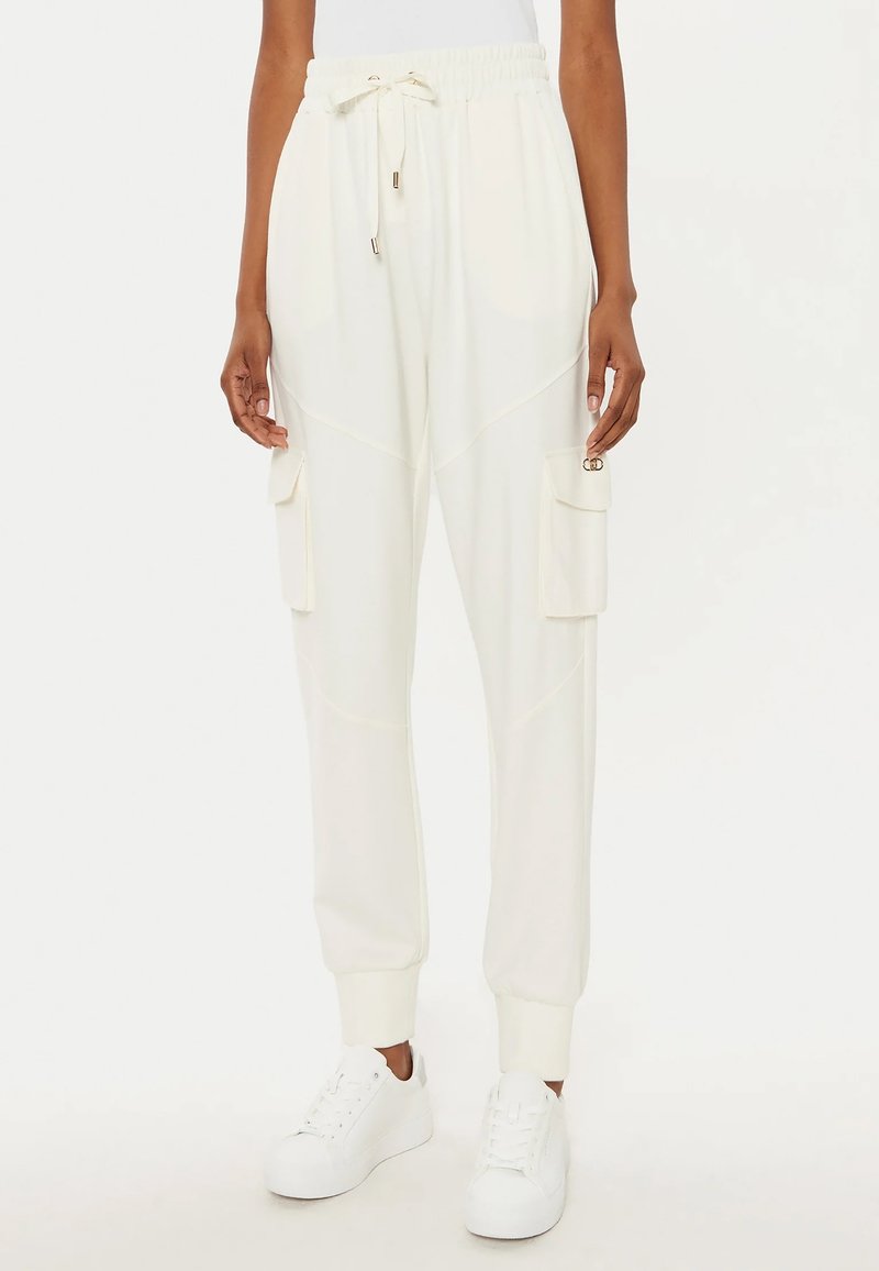 Pantaloni jogger bianchi con vita elasticizzata, tasche laterali, orli a costine e cuciture piatte per una vestibilità rilassata. Abbinati a sneakers bianche.