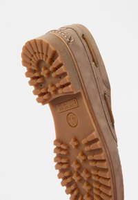 Παπούτσια Timberland με μπεζ σουέτ επάνω, καφέ καουτσούκ σόλα με υφή πυραμιδοειδών μοτίβων και μεταλλικές θηλιές για τα κορδόνια.