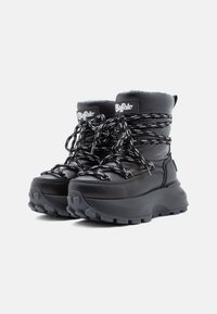 Pár černých zimních bot Buffalo s tlustými podrážkami a černo-bílými tkaničkami, vystavených na jednobarevném bílém pozadí.