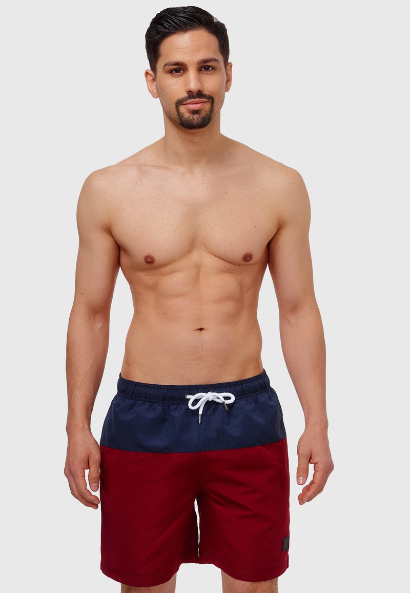 Shorts de bain rouges et navy avec une taille élastique, un cordon blanc et des poches latérales. Présente un design uni et un tissu texturé.