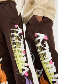 Bruna träningsoverallsbyxor med livliga, abstrakta grafik i vitt, rosa, grönt och blått. Elastisk midja med sidofickor.