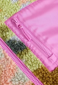 Texturerad, flerfärgad fleece i rosa, grön och brun med en rosa dragkedjedetalj längs sömmen, som visar en blandning av mjuka fibrer och slät tyg.