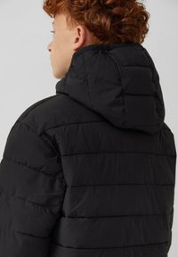 Gewatteerde zwarte jacket met capuchon, voorzien van zichtbare horizontale stiklijnen en een gladde textuur. Ontworpen voor warmte en isolatie.