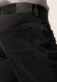 Vaqueros de denim negro con una textura suave, que presentan una etiqueta de cuero con la inscripción "BOSTON PARK" en la parte trasera y un único bolsillo trasero.