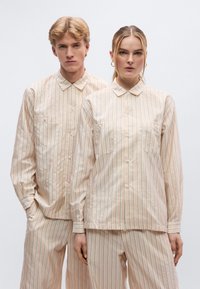 Φανέλα και παντελόνι σε ανοιχτό μπεζ με ρίγες, με κουμπιά, γιακά και εμπρόσθιες τσέπες με κάθετες ρίγες σε μπλε και πράσινο.