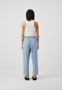 Light blue, loose-fitting trousers with an elastic waistband, paired with a white ribbed tank top. The look features a minimalist design.