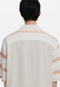 Korte mouwen shirt met een gestructureerd crèmekleurig lichaam en meerkleurige strepen in oranje en blauw over de schouders, met een kraag.