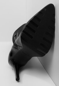 Bota de tacón alto negra con punta estrecha, parte superior de cuero liso y suela de goma texturizada con ranuras horizontales. Detalle de cremallera en el costado.