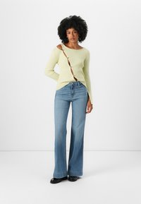 Maglione ribbed giallo chiaro con un taglio unico e dettagli di bottoni, abbinato a jeans blu a gamba larga e scarpe nere flat.