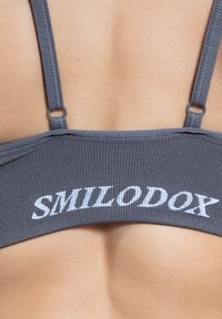 Grau Sport-BH mit gerippter Textur, mit dünnen Trägern und dem Schriftzug "SMILODOX" in weißer Schrift auf dem Bund.