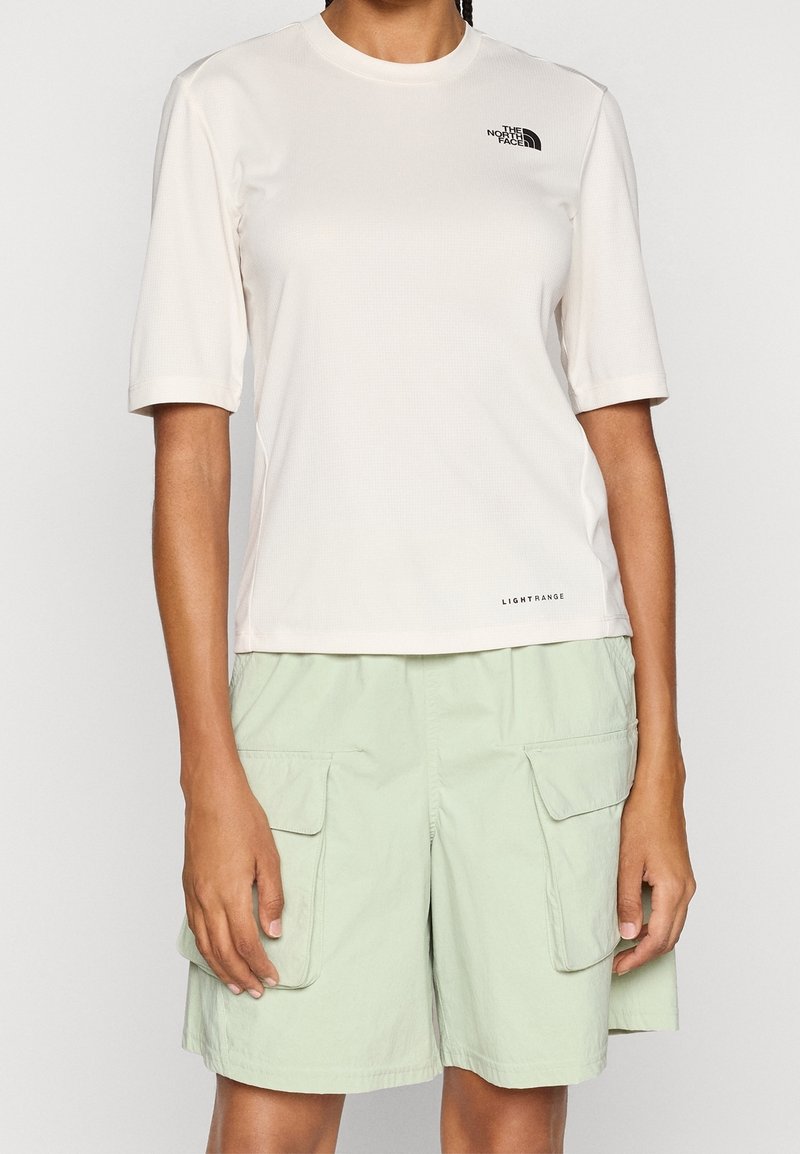 Lehké krémové tričko s krátkým rukávem, texturovaným povrchem a malým černým logem. Kombinováno s mátově zelenými kraťasy s kapsami po stranách.