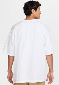 Camiseta blanca de gran tamaño hecha de algodón. Presenta mangas cortas, un escote redondo y una textura suave y lisa. La vista trasera muestra hombros caídos.