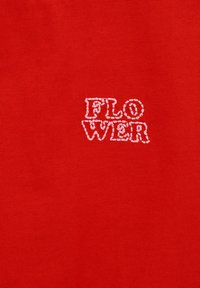 Tissu rouge avec des lettres blanches brodées formant le mot "FLOWER" en deux lignes, centrées sur le matériau.