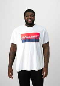 White cotton T-shirt featuring a bold red and blue "JACK&JONES" graphic. Short sleeves, crew neck, relaxed fit. Smooth texture.