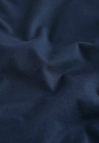 Tissu bleu foncé avec une texture subtile de tissage diagonal, légèrement froissé et plié, montrant des variations de lumière et d'ombre.