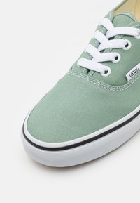Grüne Canvas-Sneaker mit weißen Schnürsenkeln, schwarzem Gummirand und einer strukturierten Oberflächenbeschaffenheit. Mit Vans-Logoschild an der Seite.