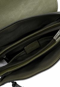 Olive zelená kožená taška uvnitř s několika kapsami, zipovými uzávěry a texturovaným povrchem; obsahuje černou textilní podšívku.