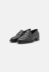 Svarta läderloafers med en texturerad vävd frampanel, platt häl och slät yta. Har en klassisk slip-on-design och minimala detaljer.