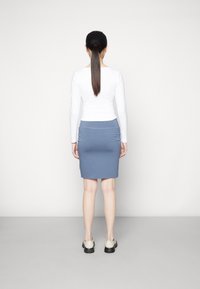 Top blanco de manga larga combinado con una falda azul ajustada, con una textura suave y de longitud hasta la mitad de la pantorrilla. Complementado con zapatos de color claro.