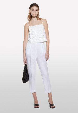 Top bianco con spalline sottili e applicazioni floreali testurizzate, abbinato a pantaloni larghi bianchi in lino e sandali neri con le dita scoperte. Borsa intrecciata nera.