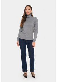 Pulover gri cu guler înalt dintr-un material moale, cu un design ajustat, asociat cu blugi bleumarin închis și pantofi cu toc ascuțit negri, cu detalii cu bretele.