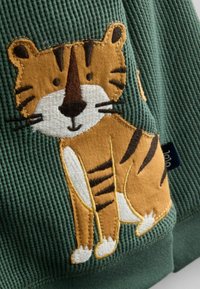 Grøn kordfløjl med et broderet tigerdesign i brun og hvid, som har striber og ansigtstræk.