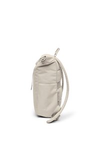 Lysebeige, slank rygsæk med polstrede skulderstropper, frontlomme og en topklaffelukning, vist stående oprejst mod en hvid baggrund.